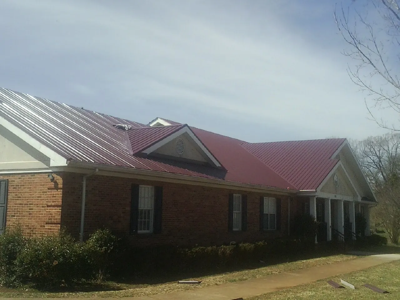 Red metal roof with gabled entries on a long brick building, from a Hail Damage Roof Repair job in Bradley