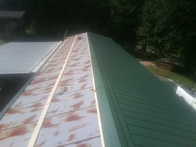 Old rusted panels beside newly installed green metal roofing — Wind Damage Roof Repair by Roofing Brothers in Bradley
