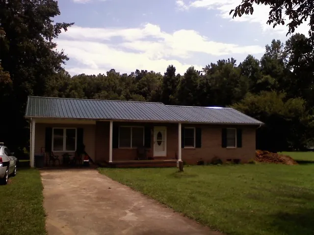Dark green metal roof on a brick ranch with a covered porch in Bradley